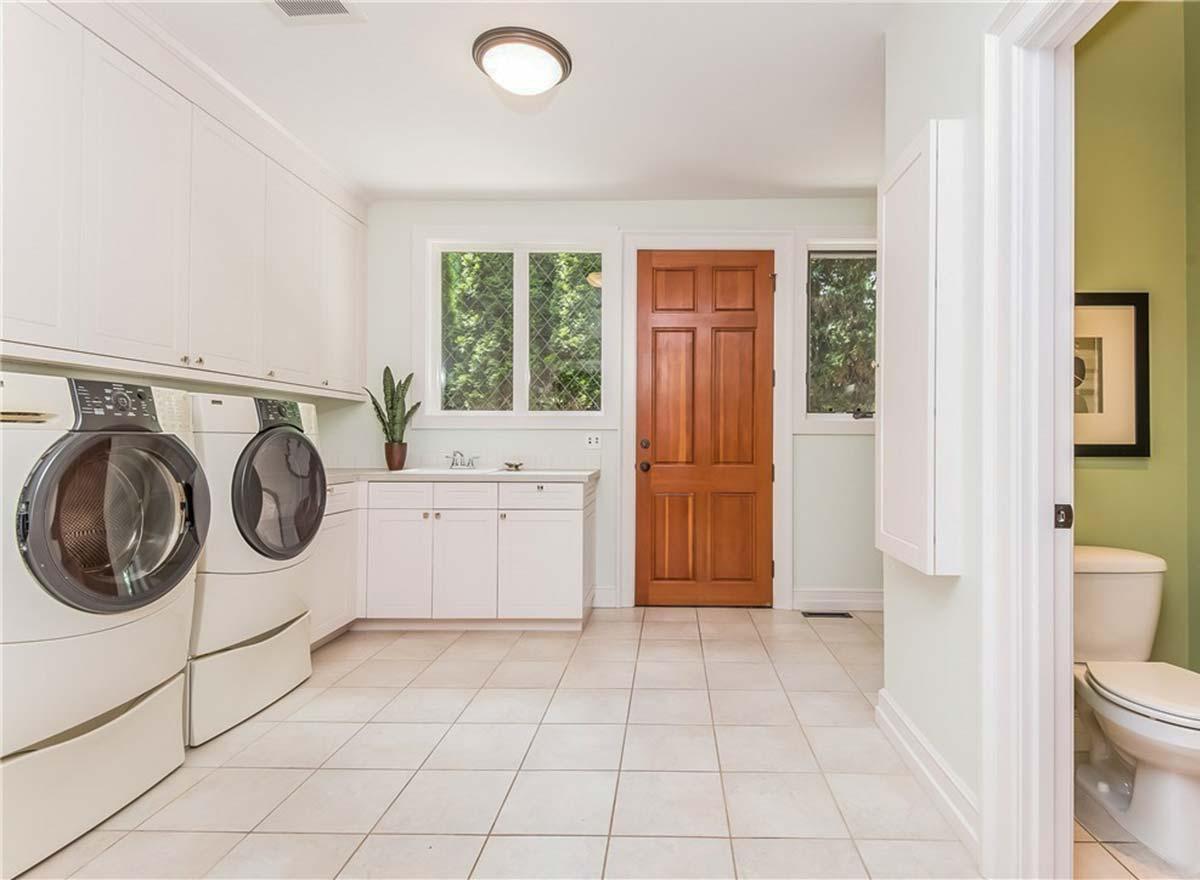 Laundry room interior with washer, dryer, sink, white cabinetry, wood door, and nearby powder room.