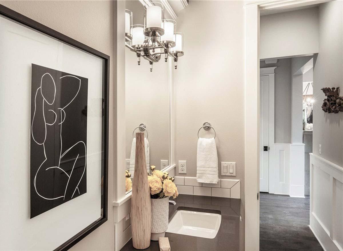 Powder room with vanity, mirror, pendant light, and framed artwork. Visible hallway with wainscoting.
