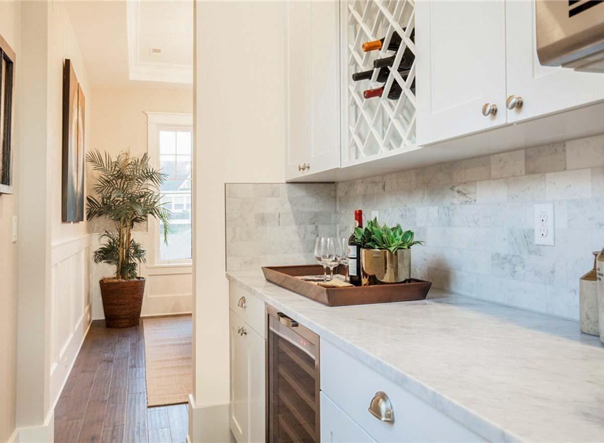 Kitchen with white cabinets, marble backsplash, wine rack, wine fridge, and tray with wine bottles and glasses.