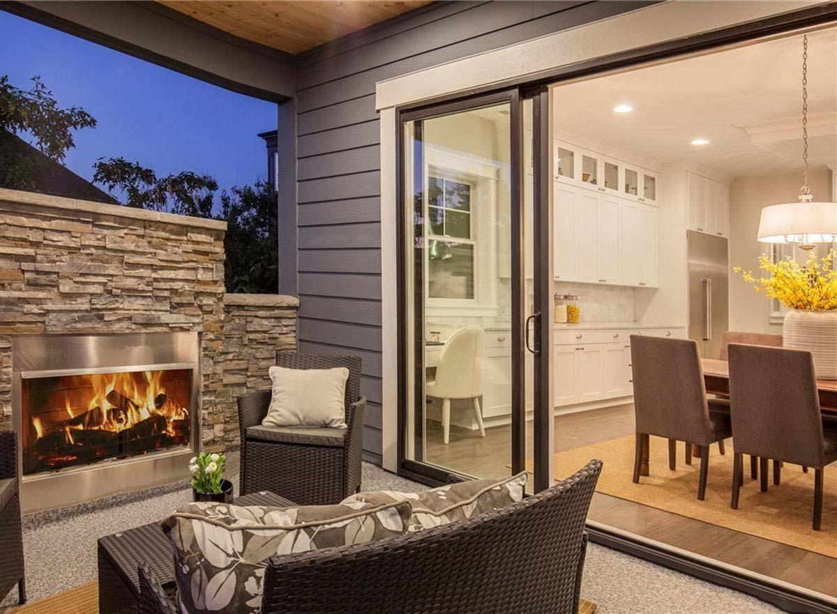 Covered patio with stone fireplace opens to dining area with white cabinets and island.