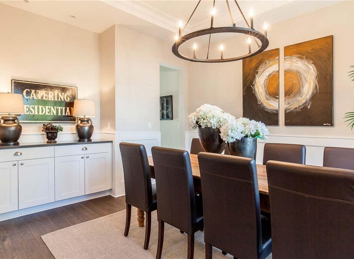Dining room with wooden table, upholstered chairs, sideboard, and circular chandelier.