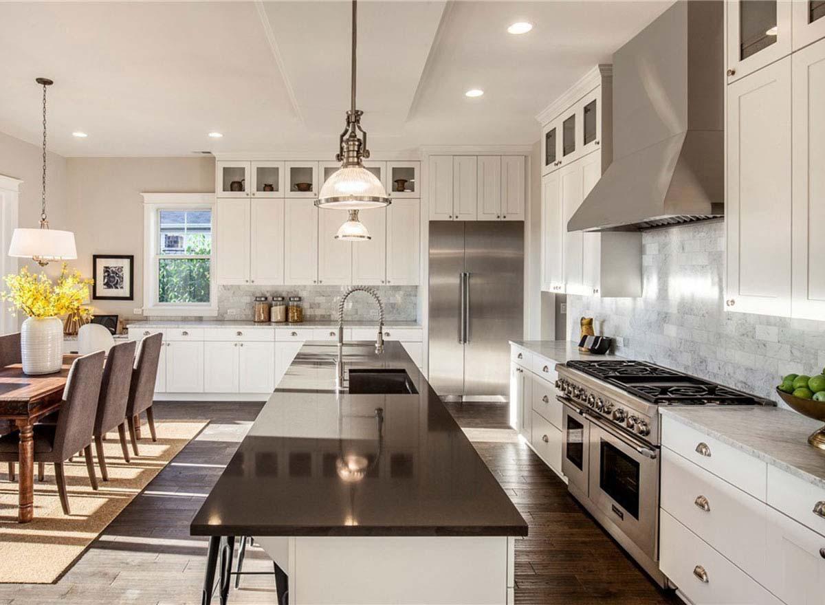 Open-concept kitchen with large island, stainless steel appliances, white cabinetry, and dining area.