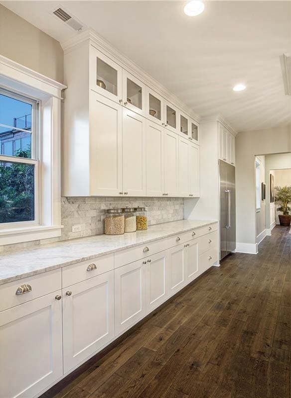Kitchen with white cabinets, marble countertops, backsplash, and stainless steel refrigerator. Dark wood floor.