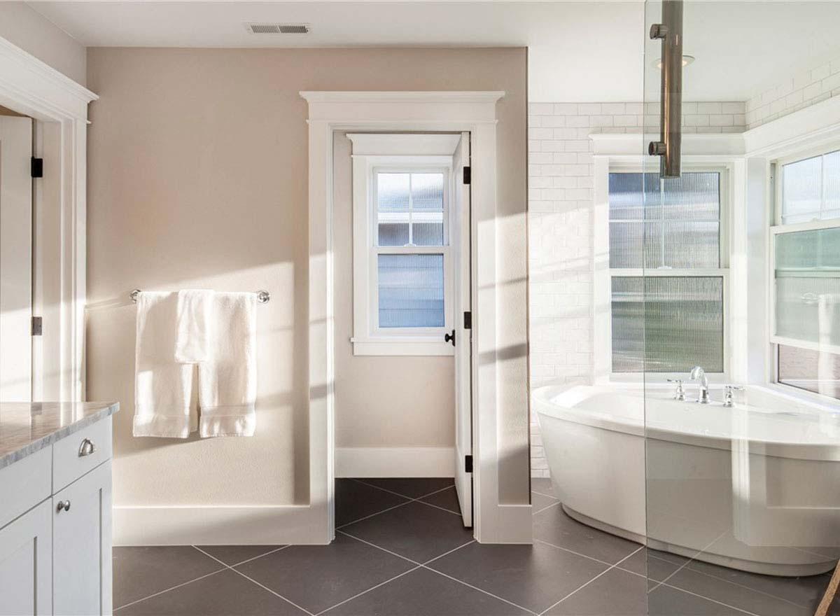 Bathroom interior with freestanding tub, subway tile wainscoting, and door leading to another room with a window.