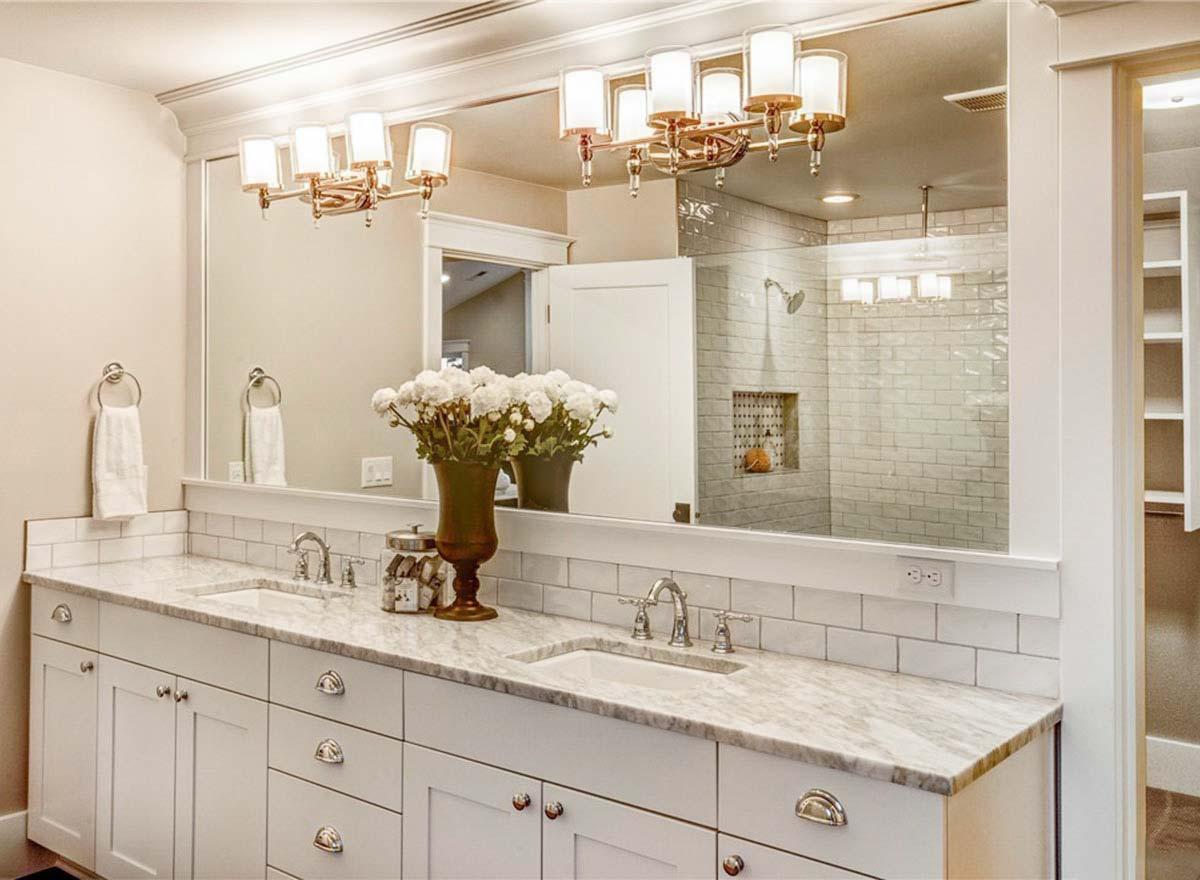 Bathroom vanity with double sinks, marble countertop, subway tile backsplash, and glass-enclosed shower with tiled walls.