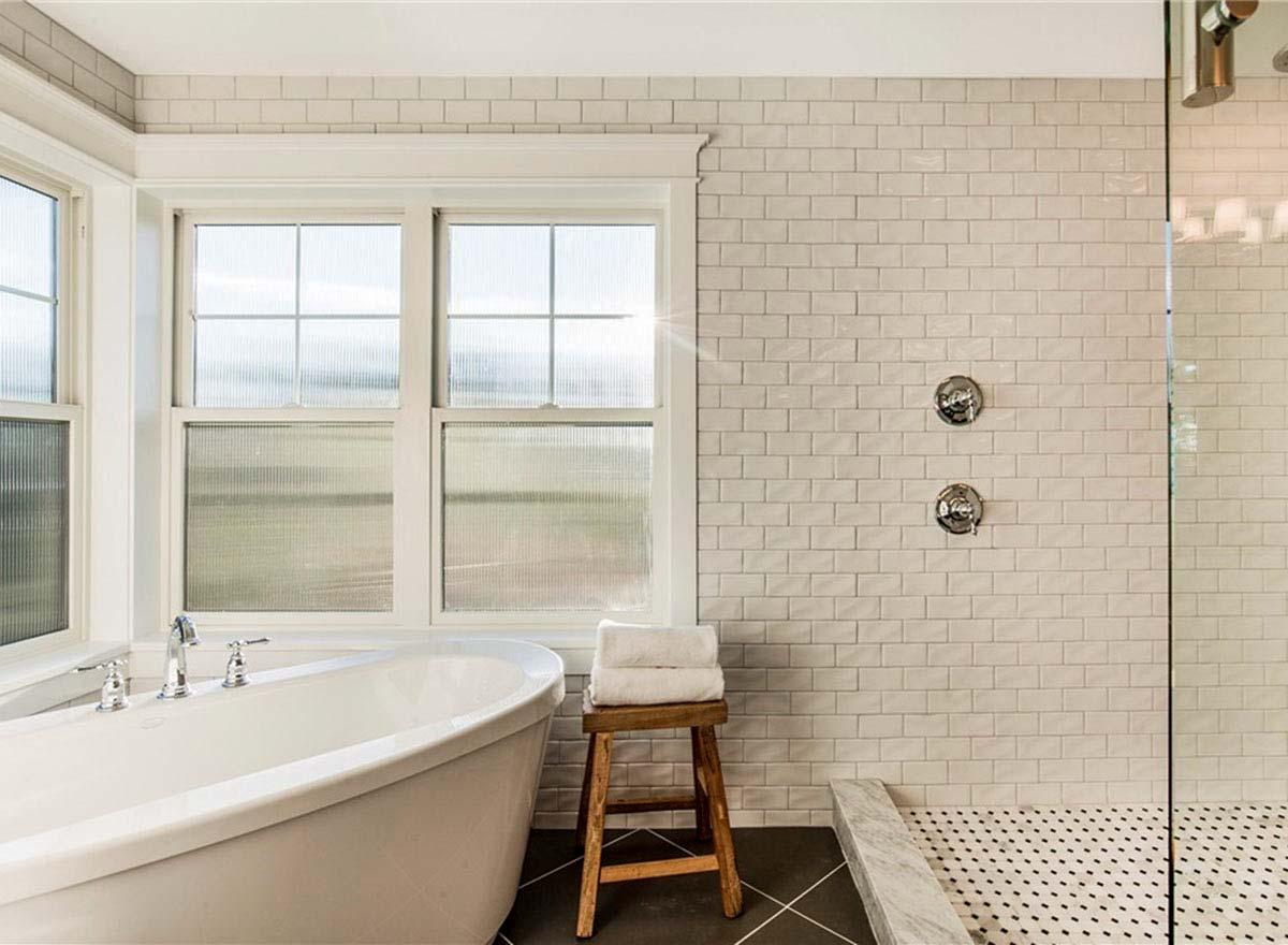 Bathroom interior with freestanding tub, shower with glass door, subway tile walls, and multi-pane windows.