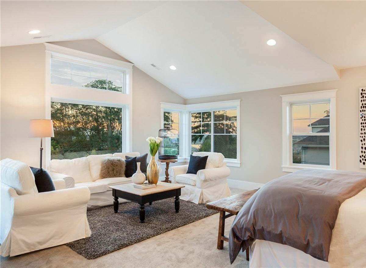 Interior view of a living space with vaulted ceiling, large windows, a sofa, chairs, and a bed.