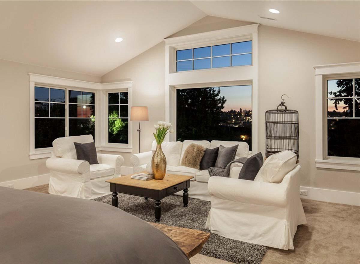 Living room with vaulted ceiling, large windows showcasing an evening cityscape, and white slipcovered furniture.