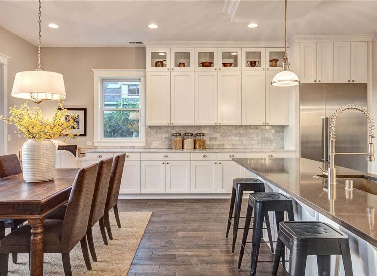 Kitchen with white shaker cabinets, marble backsplash, island with bar stools, and adjacent dining area.