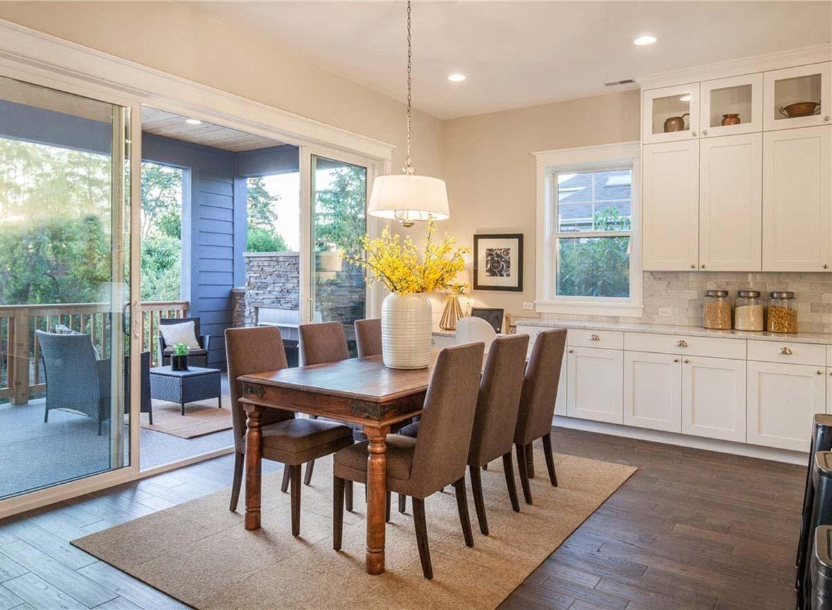 Dining area with wooden table, upholstered chairs, and white kitchen cabinets with glass fronts.