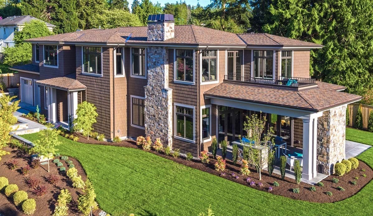 House plan exterior with stone chimney, shingle siding, multiple gables, and covered patio.