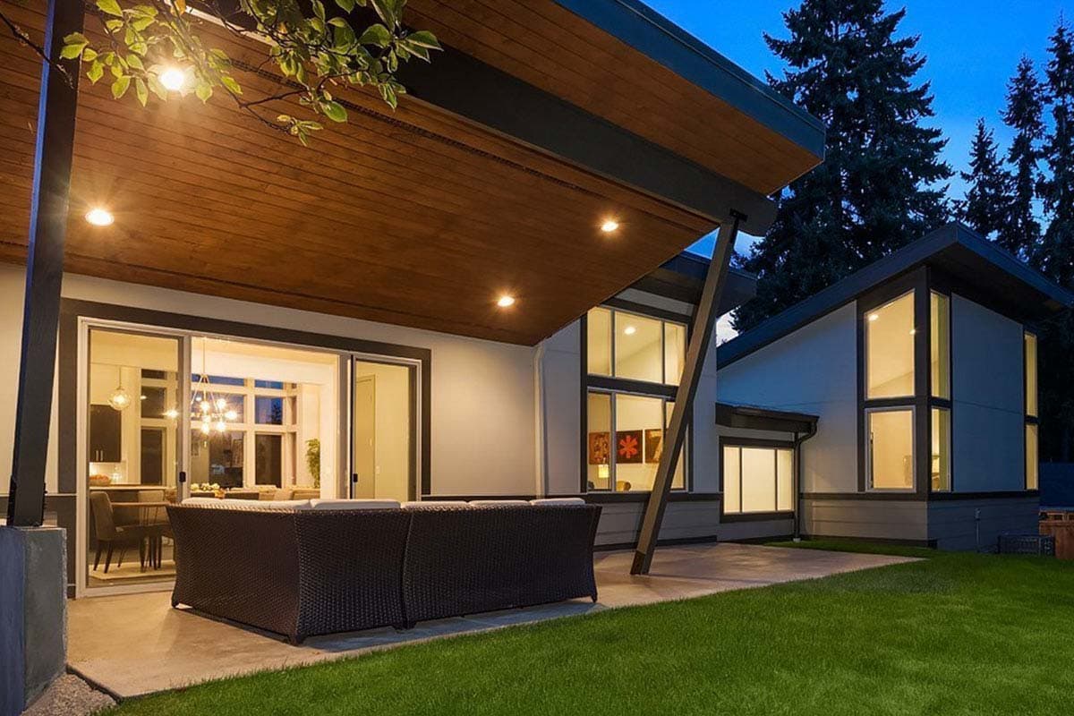 Modern house exterior with deep eaves, large windows, sloped rooflines, and covered patio.