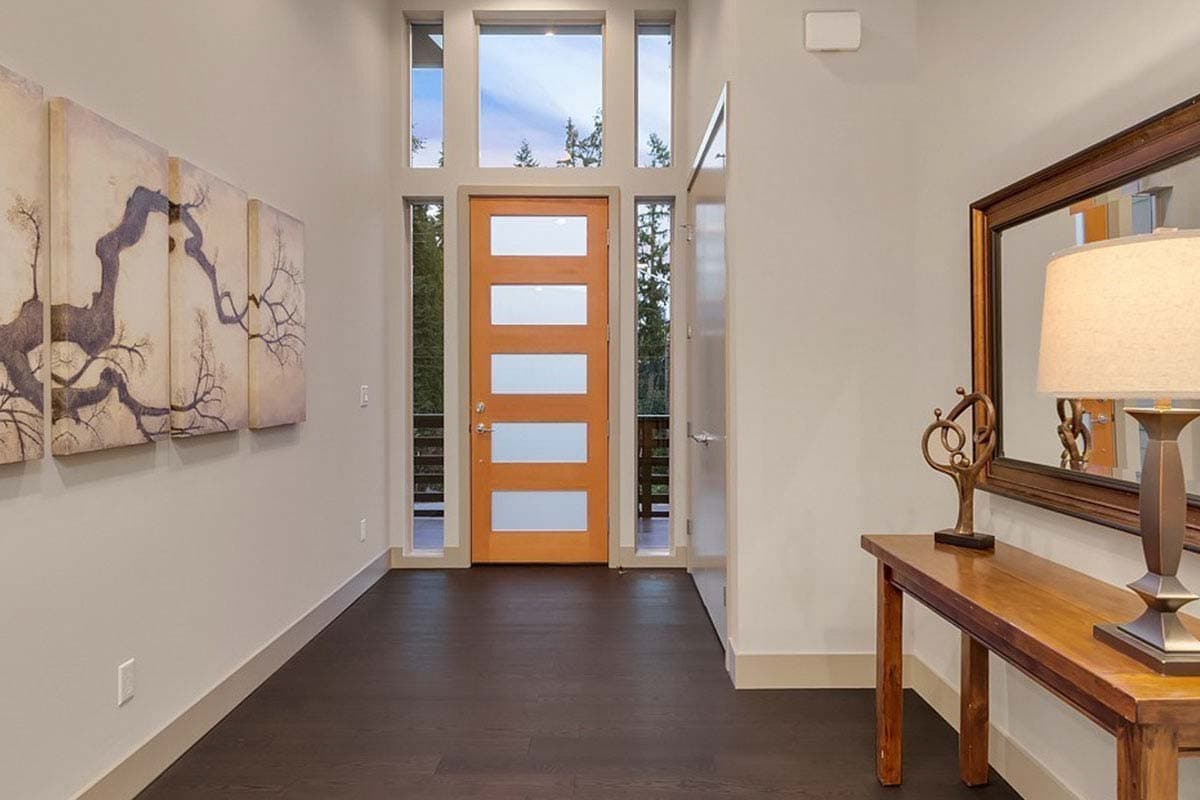 Modern entryway with wood door featuring glass panels, tall windows, and dark wood flooring.