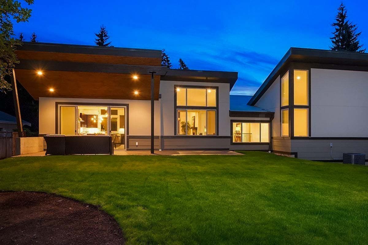 Modern house exterior with multiple gables, large windows, covered patio with wood soffit, and stucco siding.