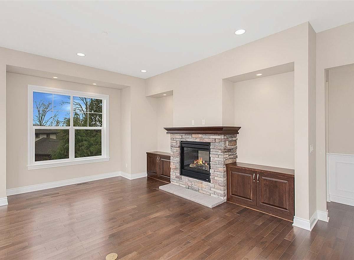 Living room with stone fireplace, flanking wood cabinets, and large window with view of trees and house.