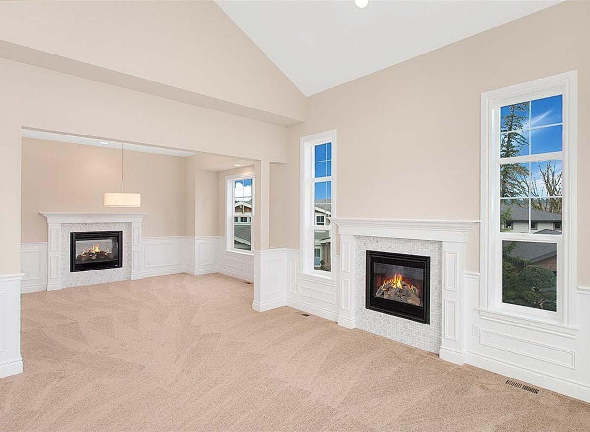 Living room with vaulted ceiling, two fireplaces, wainscoting, and large windows.