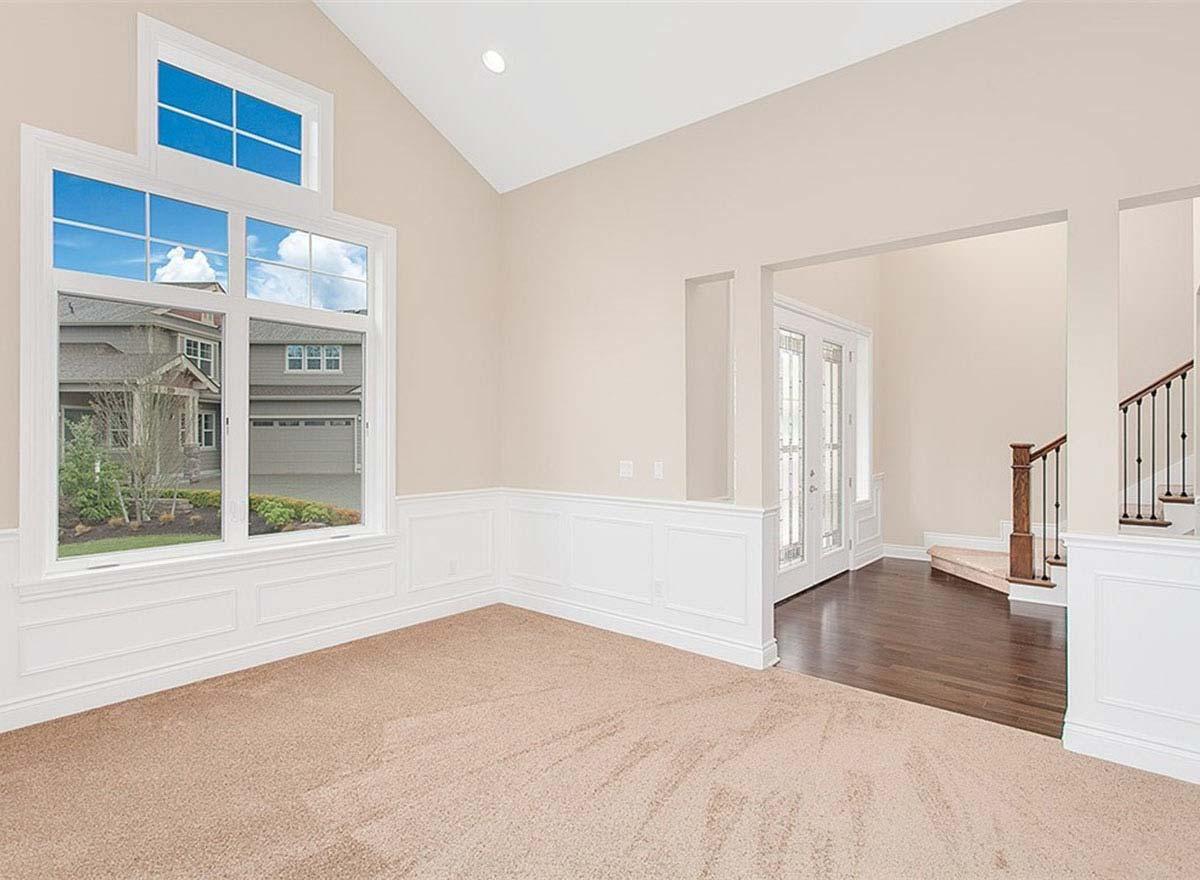 Interior view of a living space with vaulted ceiling, large multi-pane window, wainscoting, and a view to the foyer with double doors and staircase.