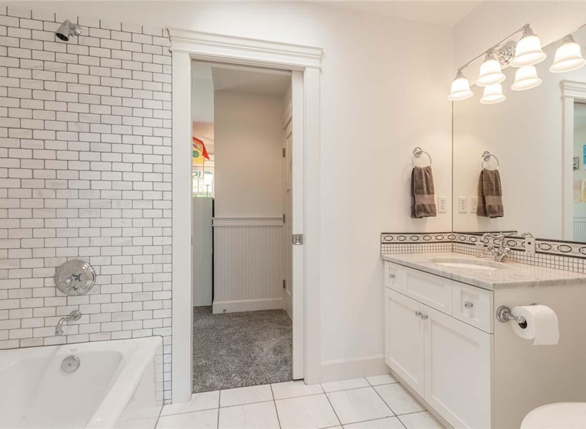 Bathroom with subway tile shower surround, white vanity with marble countertop, and tiled floor. Doorway reveals carpeted hallway.