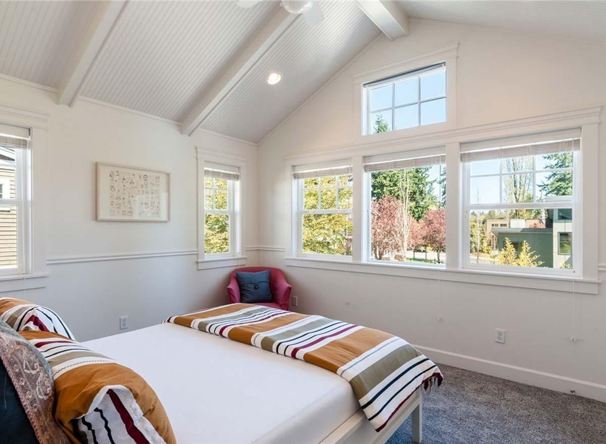 Bedroom with vaulted, beamed ceiling, multiple windows, and a striped blanket on the bed.