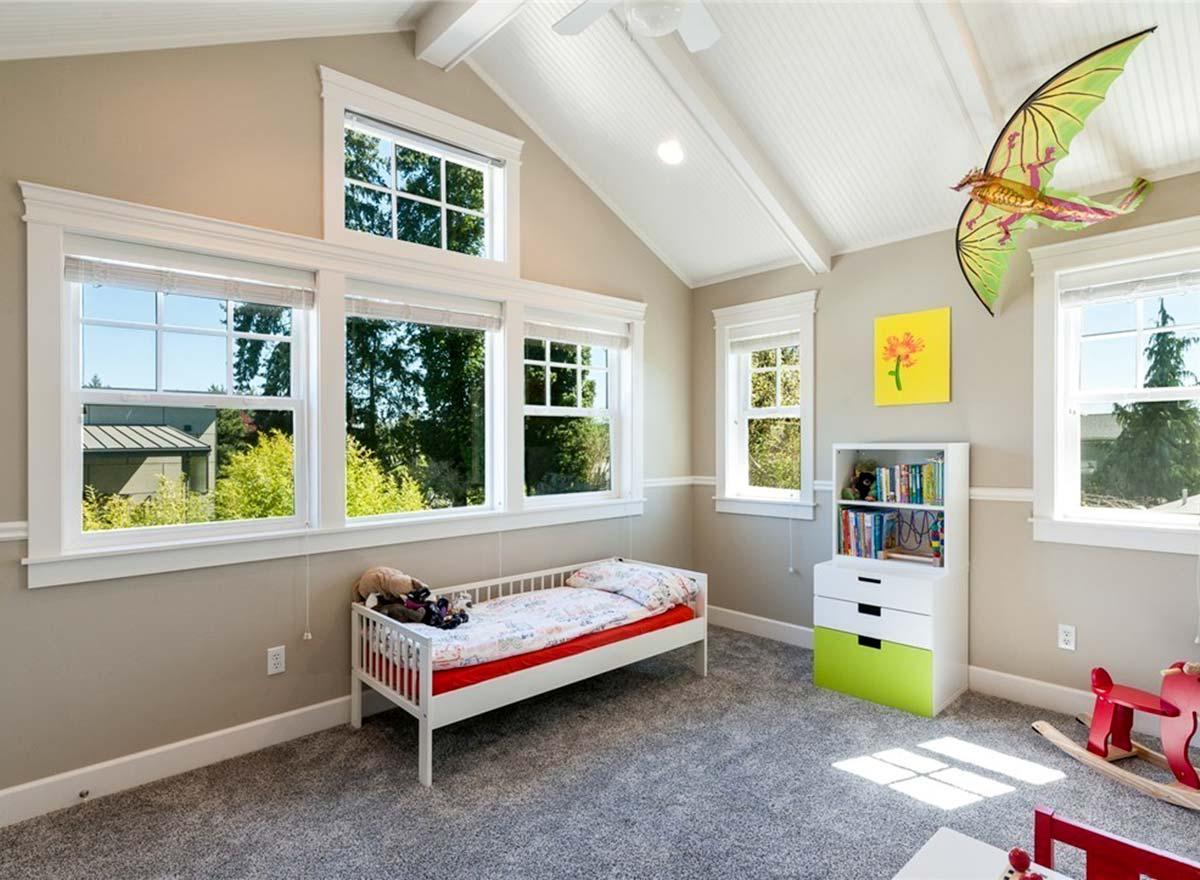Interior view of a child's bedroom with a vaulted ceiling, exposed beams, a daybed, and multiple windows.