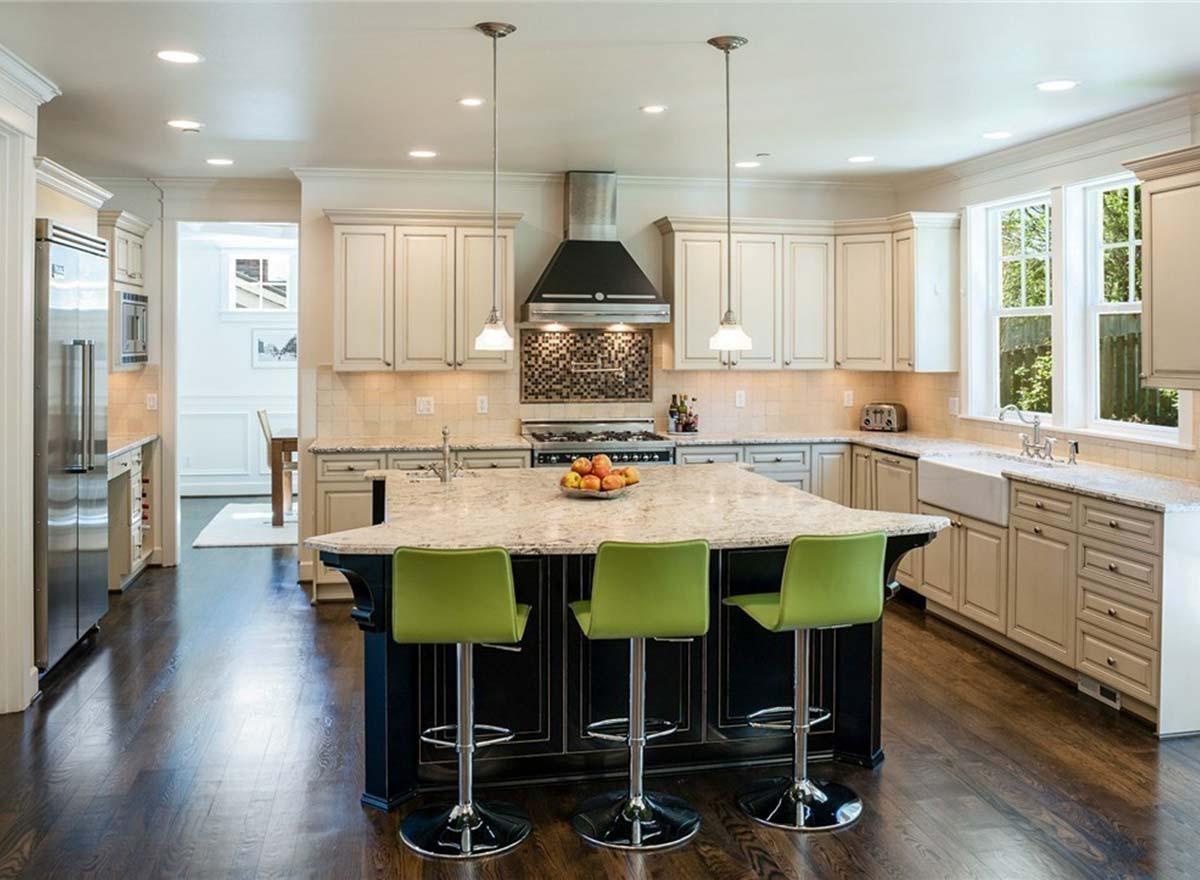 Kitchen with island, range hood, farmhouse sink, cream cabinetry, granite countertops, and dark wood floors.
