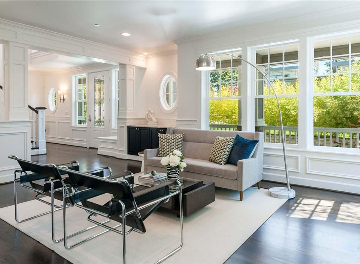 Interior view of a living room with a sofa, coffee table, chairs, and large windows overlooking a porch and trees.