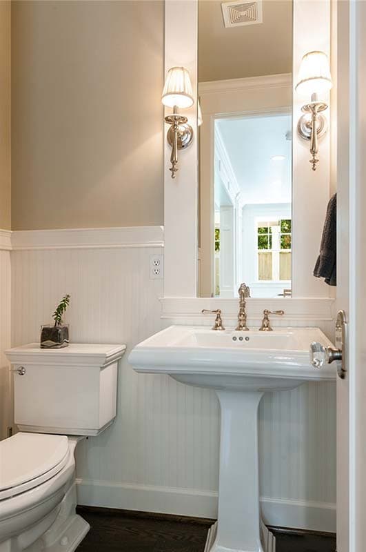 Powder room with pedestal sink, dual wall sconces, beadboard wainscoting, and a toilet.