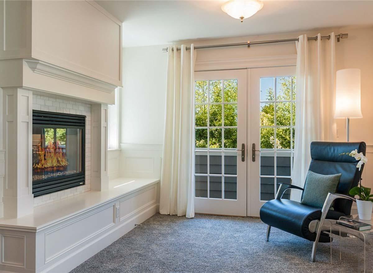 Living room with fireplace, built-in bench, and double French doors leading outdoors. Modern chair and floor lamp.