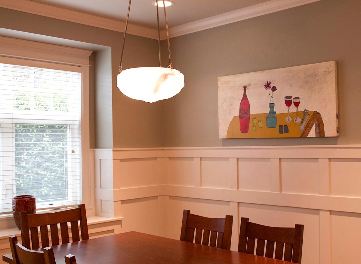 Dining room interior with wooden table and chairs, wainscoting, a window, and a pendant light.
