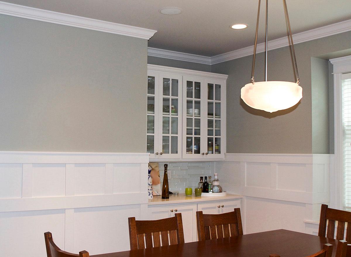 Interior dining area with wainscoting, built-in white cabinetry, glass-front cabinets, and pendant light.