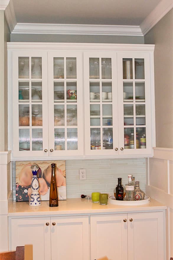 Built-in cabinetry with fluted glass upper doors and white lower doors, featuring a quartz countertop and light blue tiled backsplash.