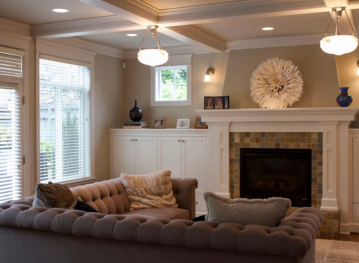 Interior view of living room with tufted sofa, fireplace, built-in cabinets, and coffered ceiling.