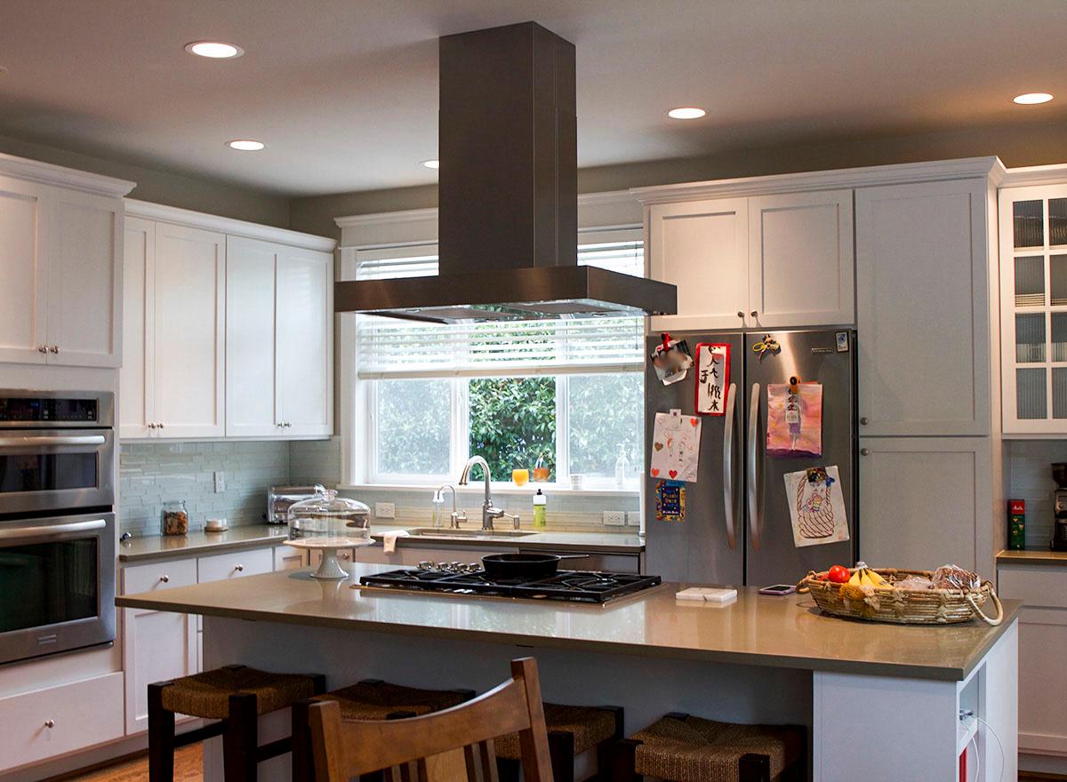 Kitchen interior with a central island featuring a gas cooktop, stainless steel appliances, white cabinetry, and a double oven.