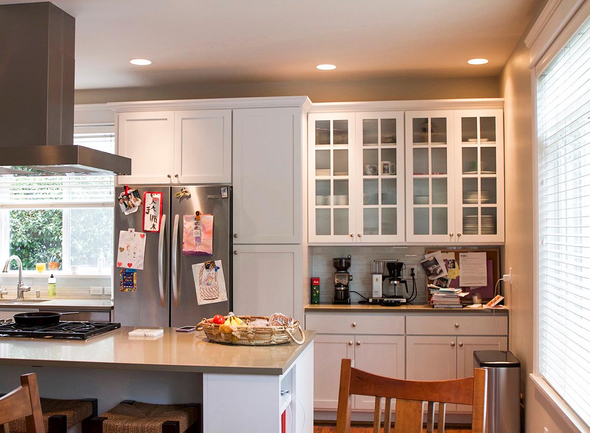 Kitchen with stainless steel refrigerator, white shaker cabinets, glass-front upper cabinets, and island.