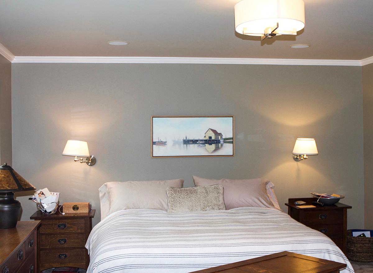 Bedroom with queen bed, two nightstands with lamps, and wall art of a boathouse.