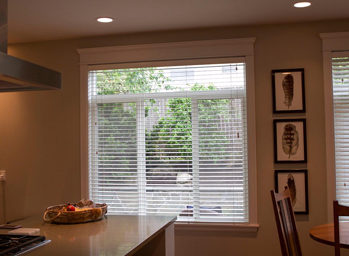 Interior kitchen view with large horizontal window, counter, and three framed feather prints on wall.