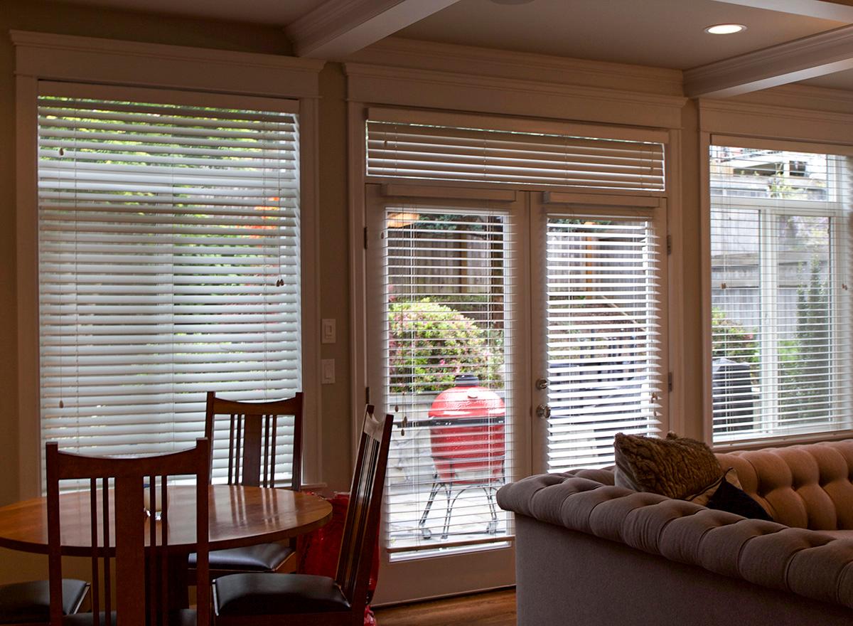 Interior view showing a dining area with chairs, a glass door leading outside to a red grill, and a tufted sofa.
