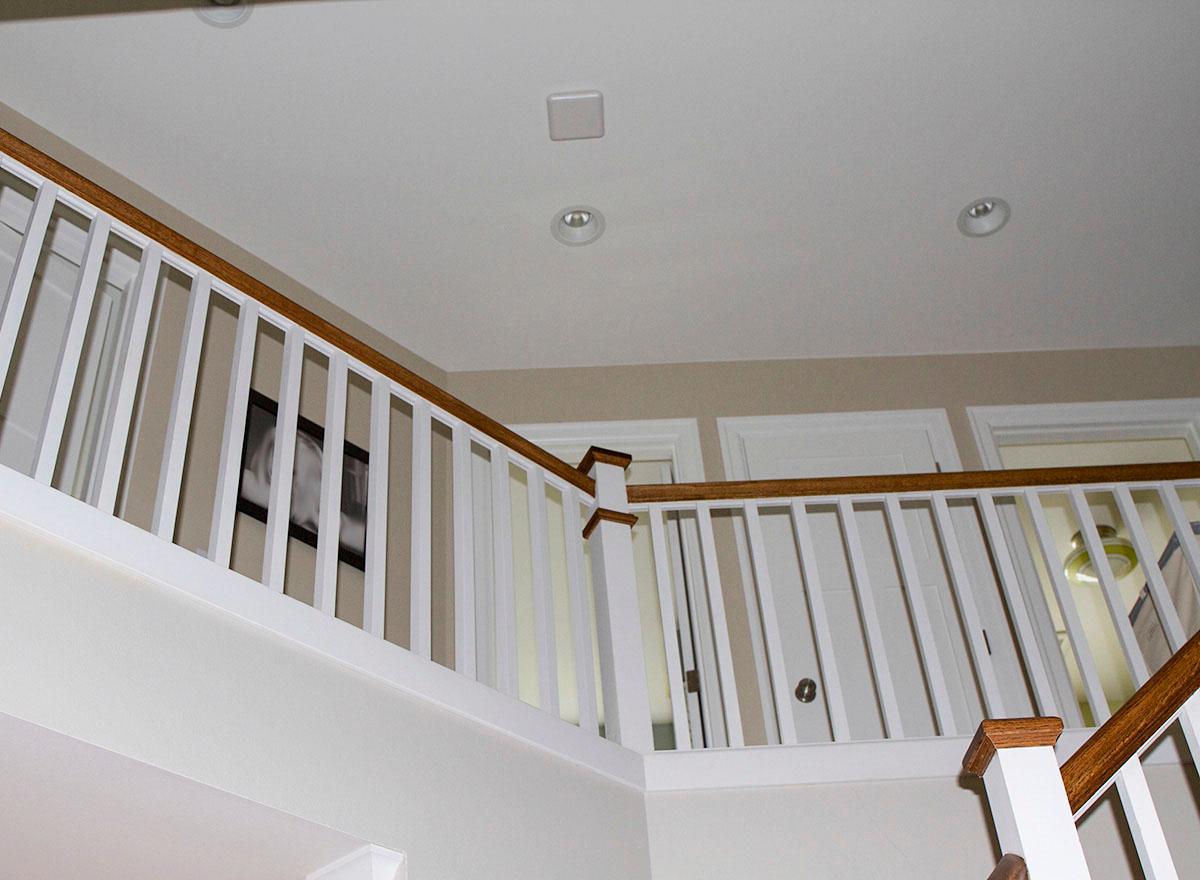 Interior view of a staircase landing with white balusters, wood handrails, and three doors visible.