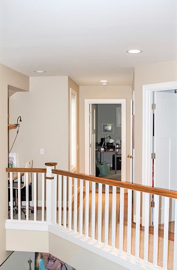 Interior view of a hallway with white railings, doors, and a desk area in the background.