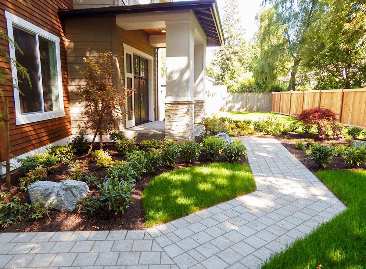 House plan exterior with wood siding, stone pillar entry, and paved walkway leading to a modern front door.