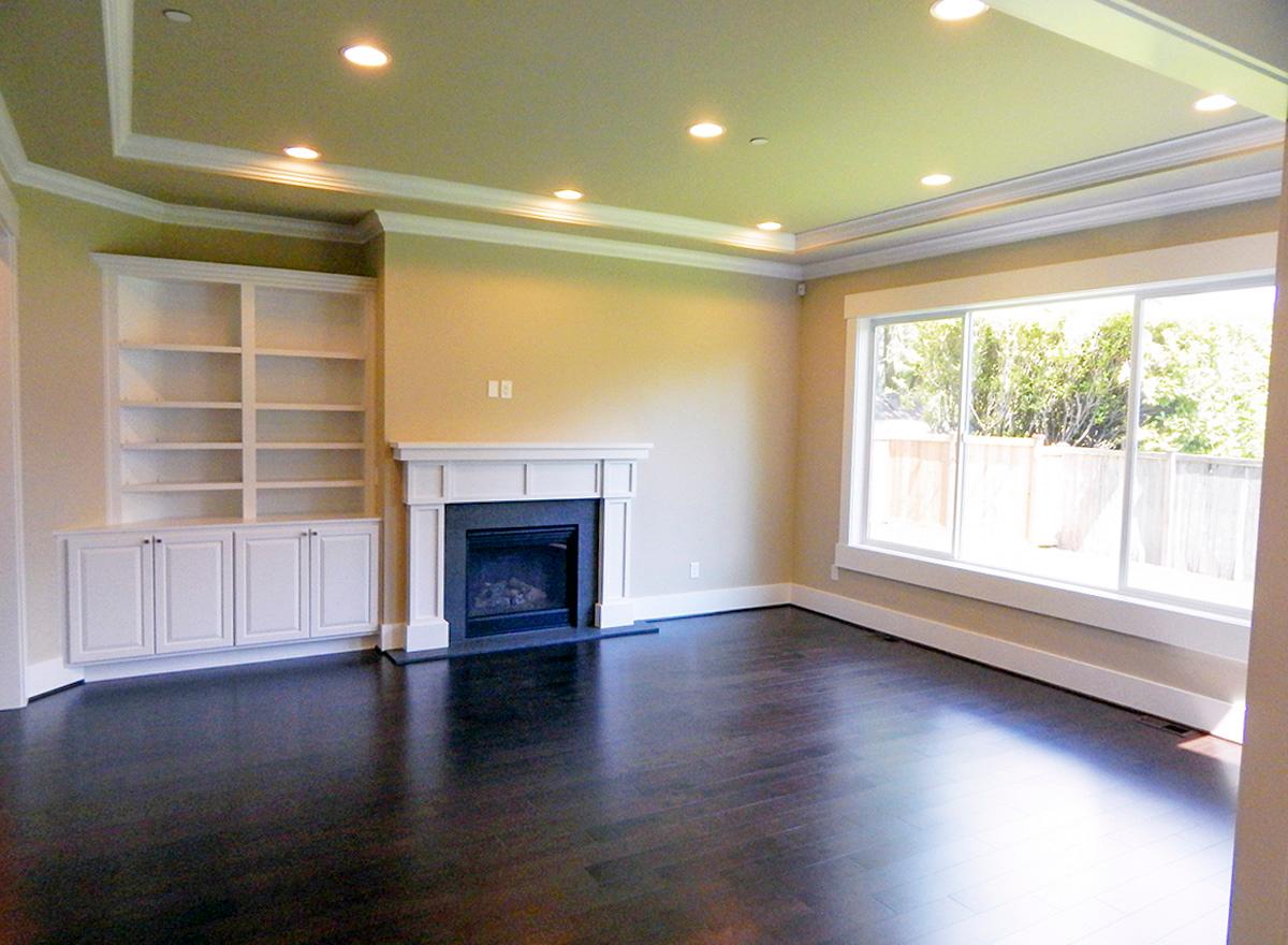 Living room with built-in bookshelves, fireplace, and large picture window with white trim. Tray ceiling with recessed lighting.