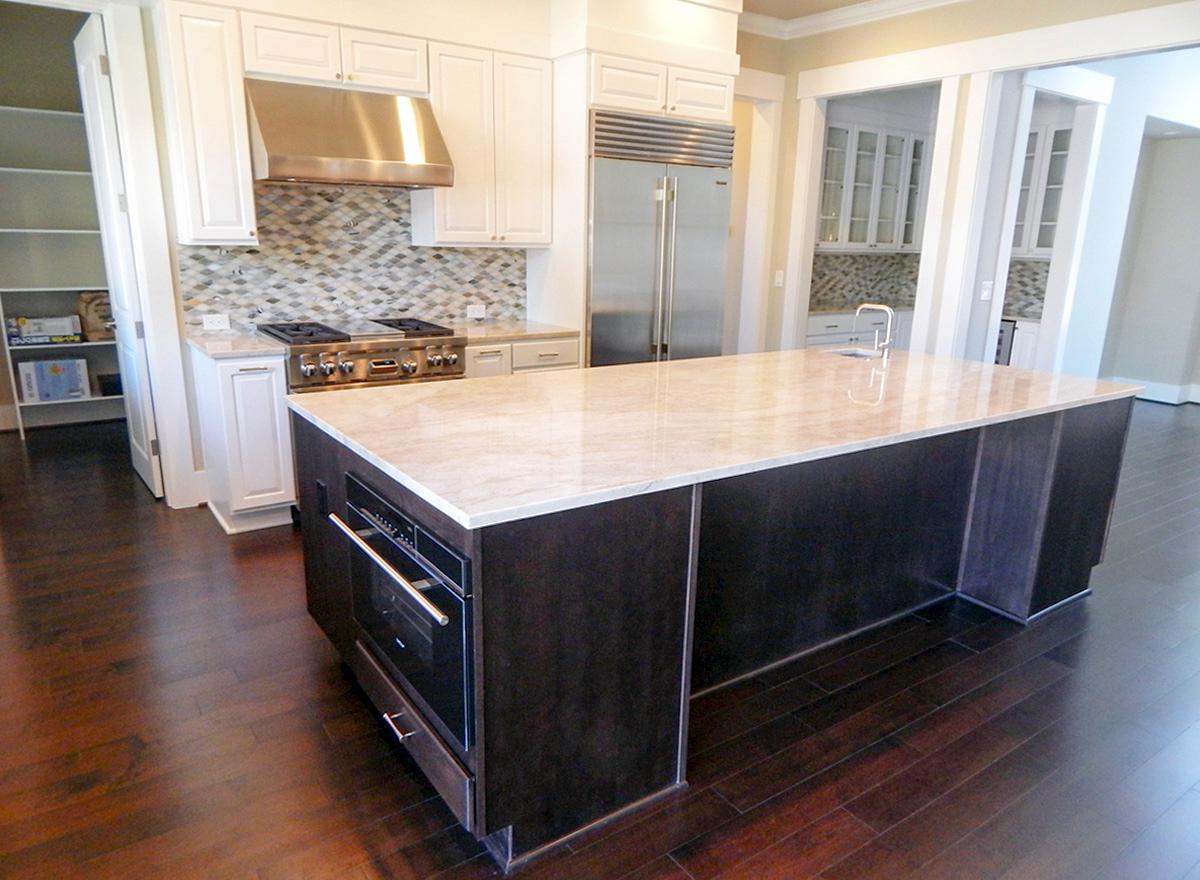 Kitchen island with built-in oven, stainless steel appliances, gas range, and backsplash.