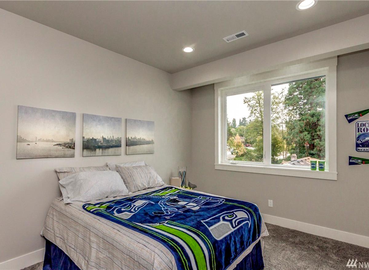Bedroom with a queen bed, three-panel city skyline art, and large casement window overlooking trees.