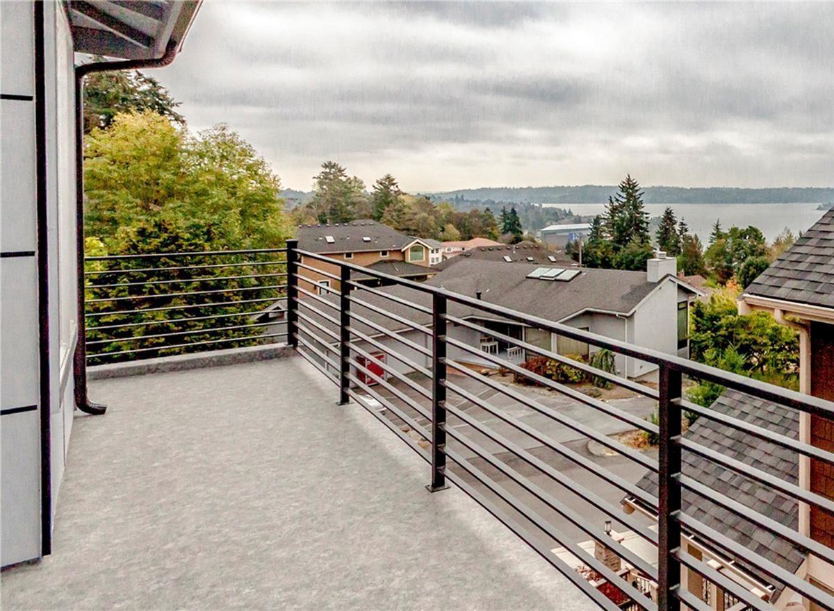 Modern house exterior with balcony, metal railing, and view of surrounding homes and water.