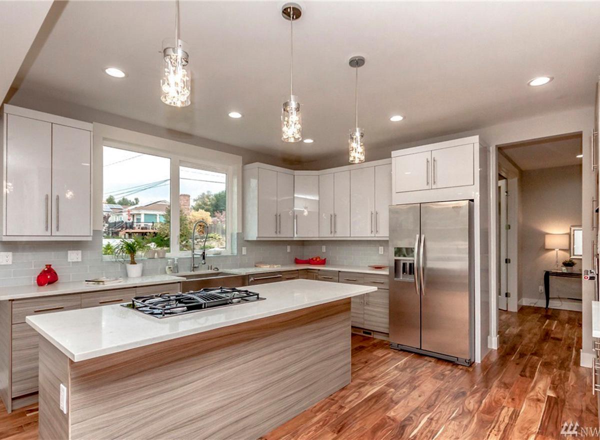 Contemporary kitchen with white cabinets, large island with gas range, stainless steel appliances, and wood floors.
