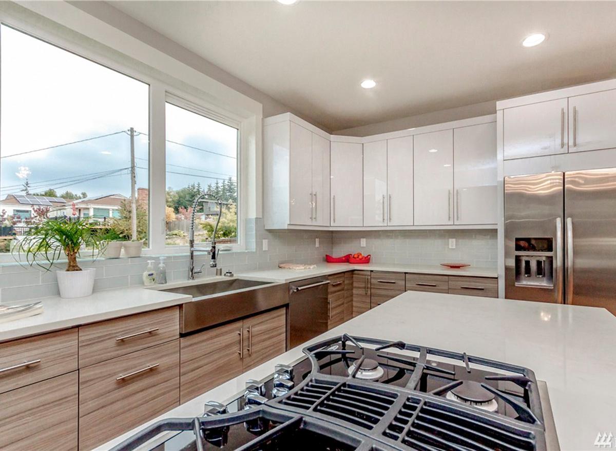 Modern kitchen with white high-gloss cabinets, stainless steel appliances, large window, and island with gas range.