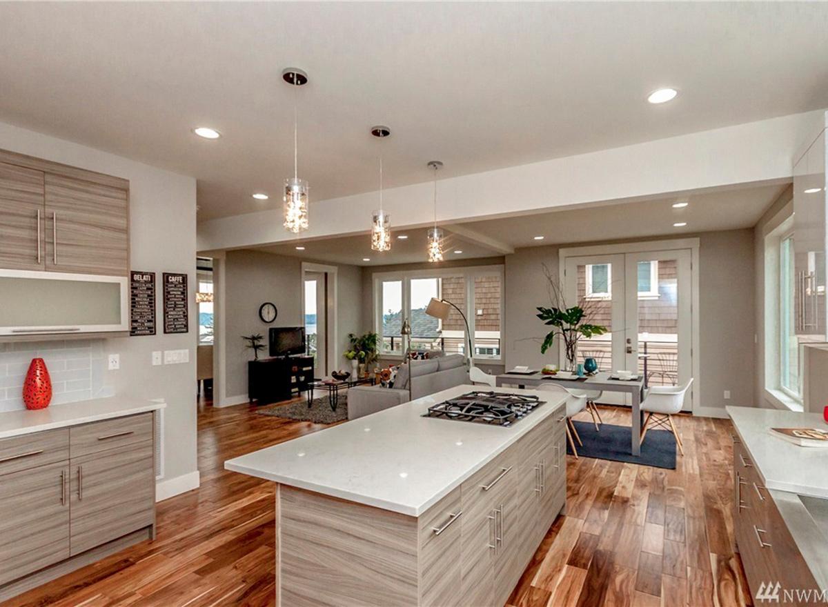 Modern kitchen with island cooktop, open to dining and living areas with large windows and glass doors.