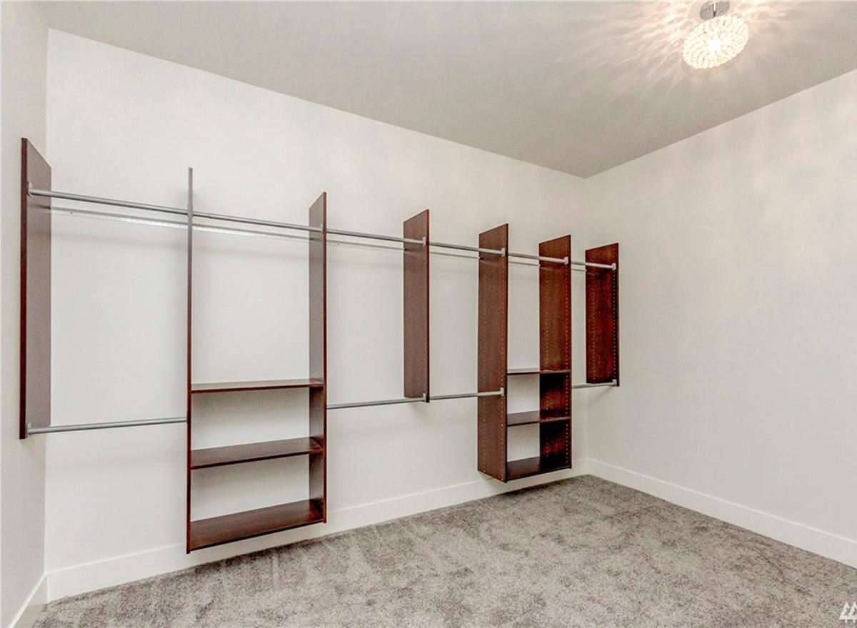 Walk-in closet with dark wood shelving units and multiple hanging rods against white walls. Gray carpet floor.