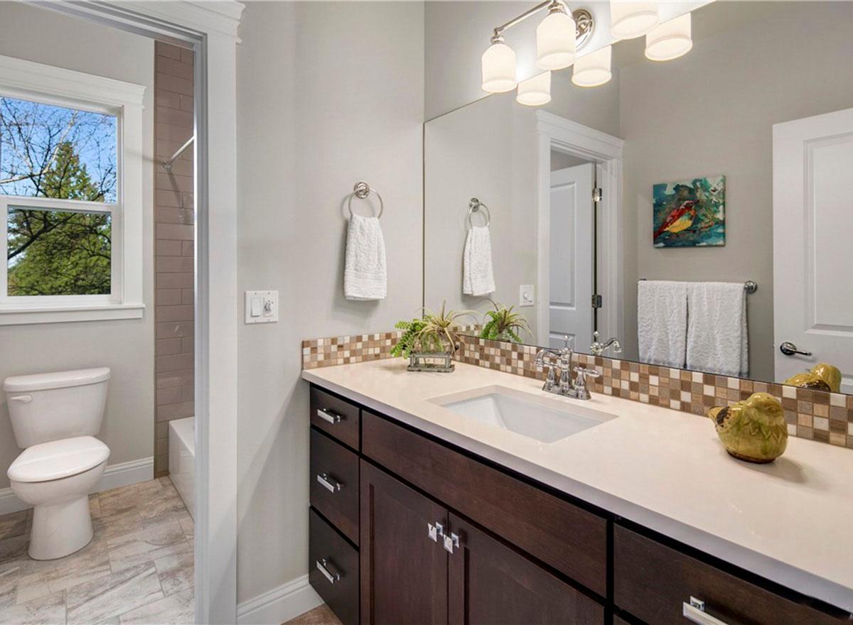 Bathroom with dark wood vanity, tiled backsplash, and separate toilet area with window.