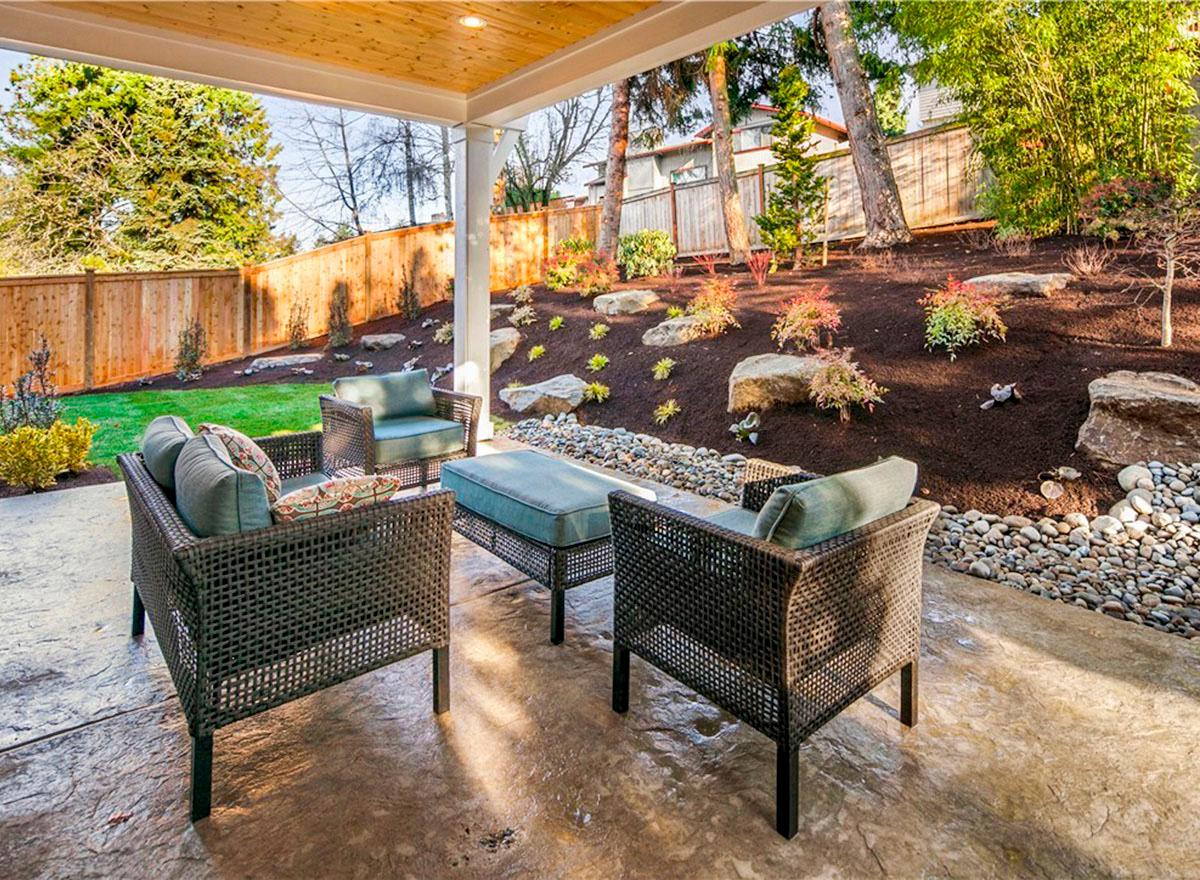 Covered patio with woven furniture, stamped concrete floor, and a landscaped yard with a wooden fence.